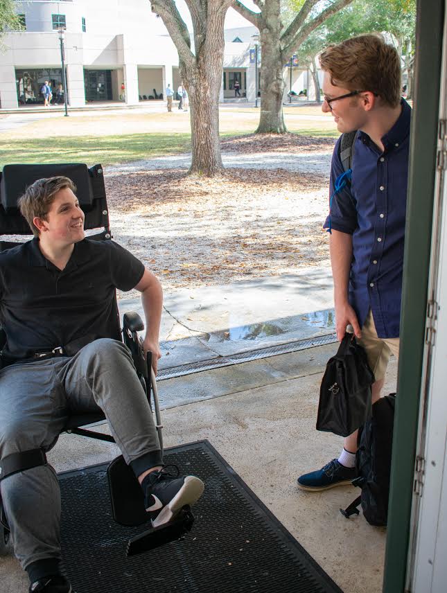 Sophomore Thomas Lightsey rolls his wheelchair into his English class as senior Robby Witten holds the door. Lightsey says that his friends are more than willing to hold open doors and push him around campus since his surgery in December.  