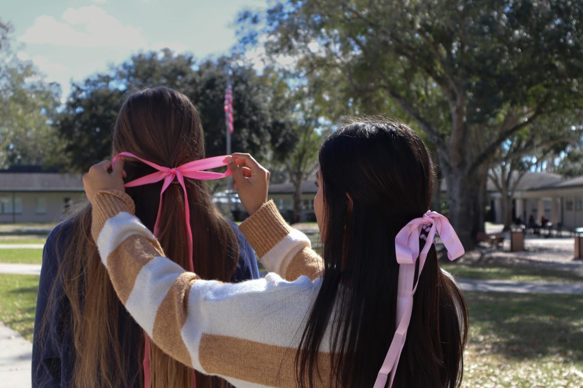 Freshman Olivia Agnew ties a pink bow into sophomore Emma Hartung’s hair. Bows, a stylish yet classic accessory, are making a comeback in the world of fashion.